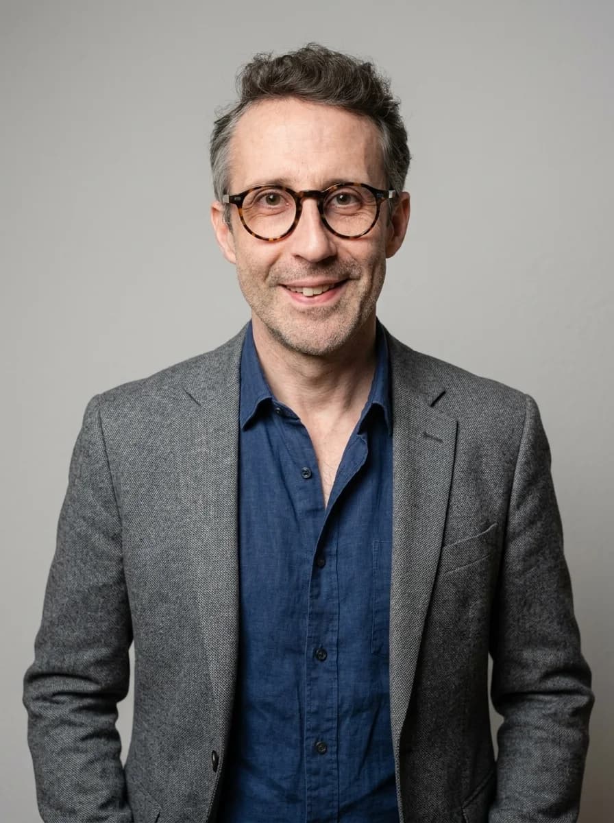 Portrait IA dentiste style corporate chaleureux - blazer gris chiné et chemise denim, sourire franc, lumière studio douce et tons chair naturels